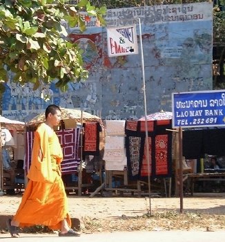 A monk walking down main road in Luang Prabang, with an old, peeling revolutionary sign in the background--and (newer) bank and email signs in the foreground
