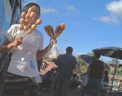 A young Lao woman selling hard-boiled eggs and roasted corn-on-the-cob-on-a-stick